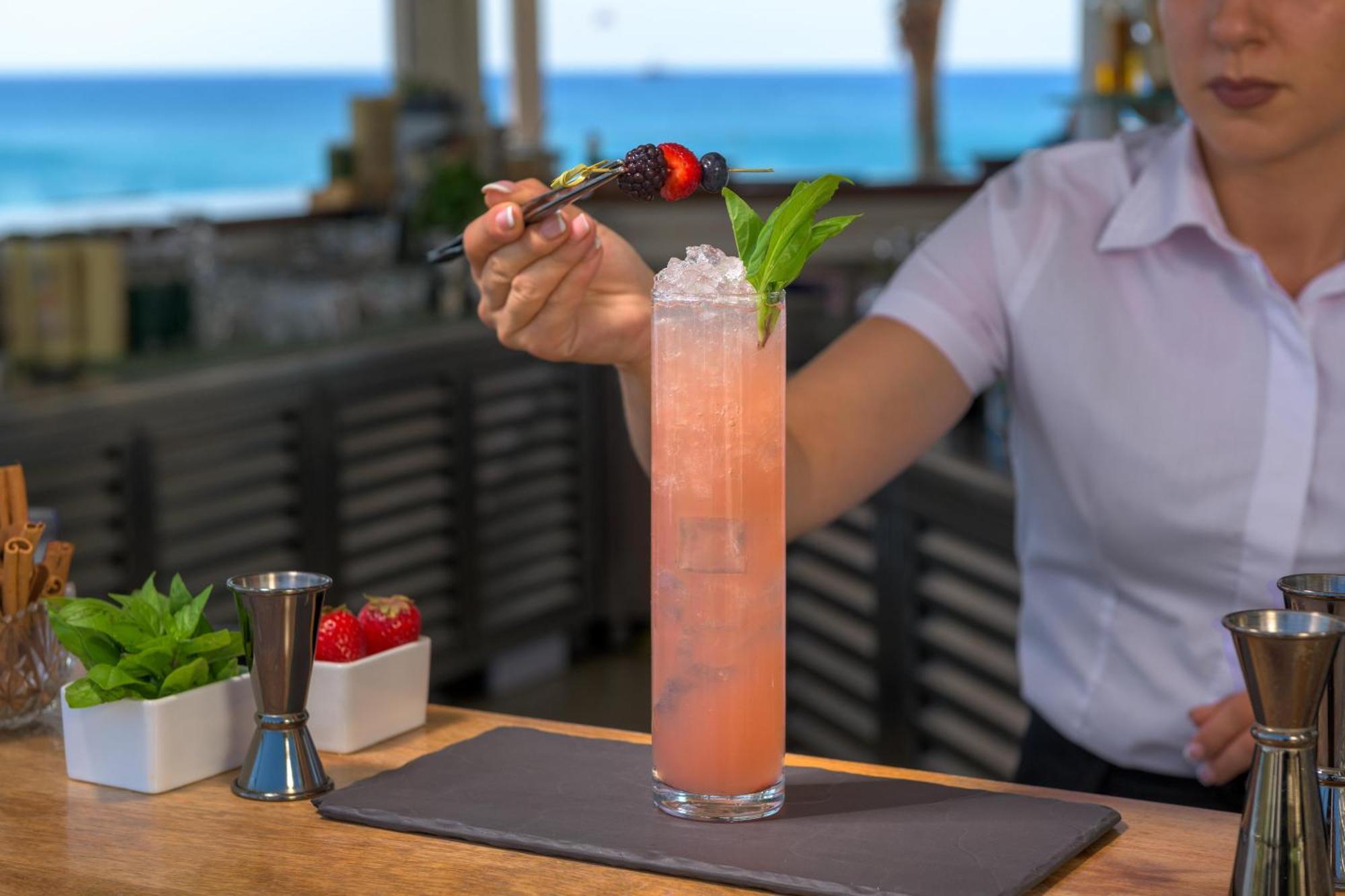 Rodos Palladium Leisure & Wellness Kallithéa Exterior foto A bartender garnishes a cocktail with a fruit skewer.